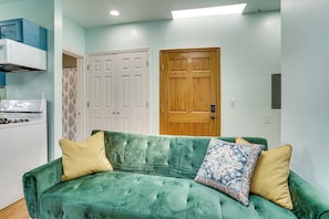 A green sofa with two pillows, a white door, and a patterned curtain in a room with light blue walls. - Walk to HBLR & Liberty State Park: Jersey City Apt (Jersey City)