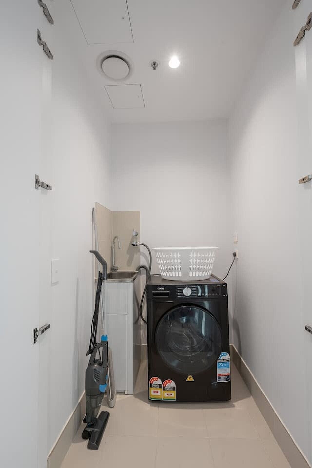 Ein kleiner Hauswirtschaftsraum mit Waschmaschine, Wäscheständer und Staubsauger.