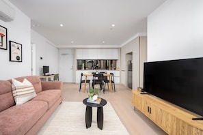 A modern living room with a sofa, a coffee table, and a TV on a wooden cabinet. - River-view balcony, free parking (Docklands)