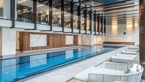 Un espace piscine intérieur moderne, doté d’une piscine à eau claire, de chaises longues et d’équipements de musculation.
