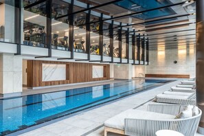 A modern indoor pool area with a clear pool, lounge chairs, and exercise equipment. - River-view balcony, free parking (Docklands)