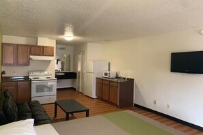 A compact living space with a kitchenette, a sofa, a small table, and a TV mounted on the wall. - 1 Queen Bed | Smoking, Kitchen, Sofa-Bed (Longview)