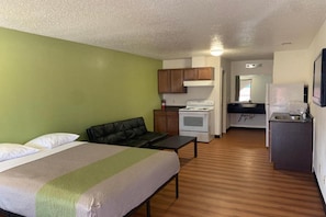 A room with a bed, a small kitchenette with a stove, and a dining area with a table and chairs. - 1 Queen Bed | Smoking, Kitchen, Sofa-Bed (Longview)