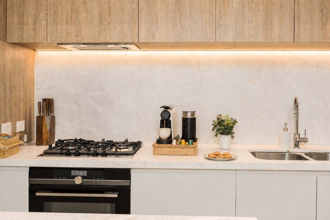 A modern kitchen with a gas stove, a built-in oven, a sink, and wooden cabinets.