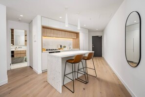 A modern kitchen with a white countertop, wooden cabinets, and two bar stools. - Sky-high pool & sauna, near Marvel (Melbourne)