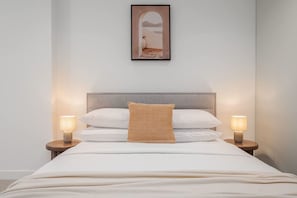 A neatly made bed with a headboard, two bedside lamps, and a framed picture above. - Sky-high pool & sauna, near Marvel (Melbourne)