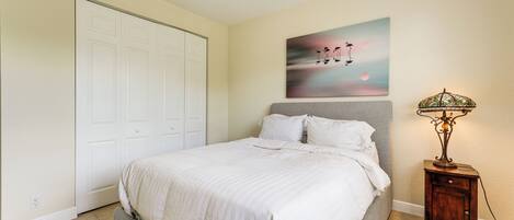 A bedroom with a bed, a nightstand, a lamp, a painting, and a closet.