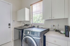 A laundry room with a washing machine, a dryer, a window with blinds, and a white cabinet.
