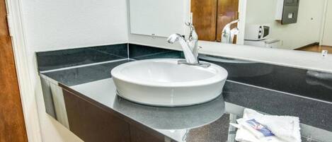 A modern bathroom with a round sink, a mirror, and a towel rack.
