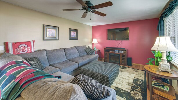 A living room with a ceiling fan, a red wall, a sofa, a coffee table, and a television. - Hot Tub, Gym & Office! Family Home in Massillon (Massillon)