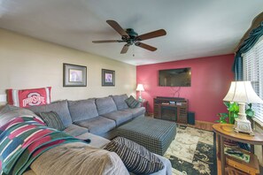 A living room with a ceiling fan, a red wall, a sofa, a coffee table, and a television. - Hot Tub, Gym & Office! Family Home in Massillon (Massillon)