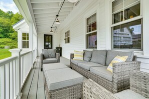 A covered porch with a wicker sofa and ottoman, a railing, and a view of the surrounding greenery. - Modern Farmhouse Between Mount Snow & Stratton! (Wardsboro)