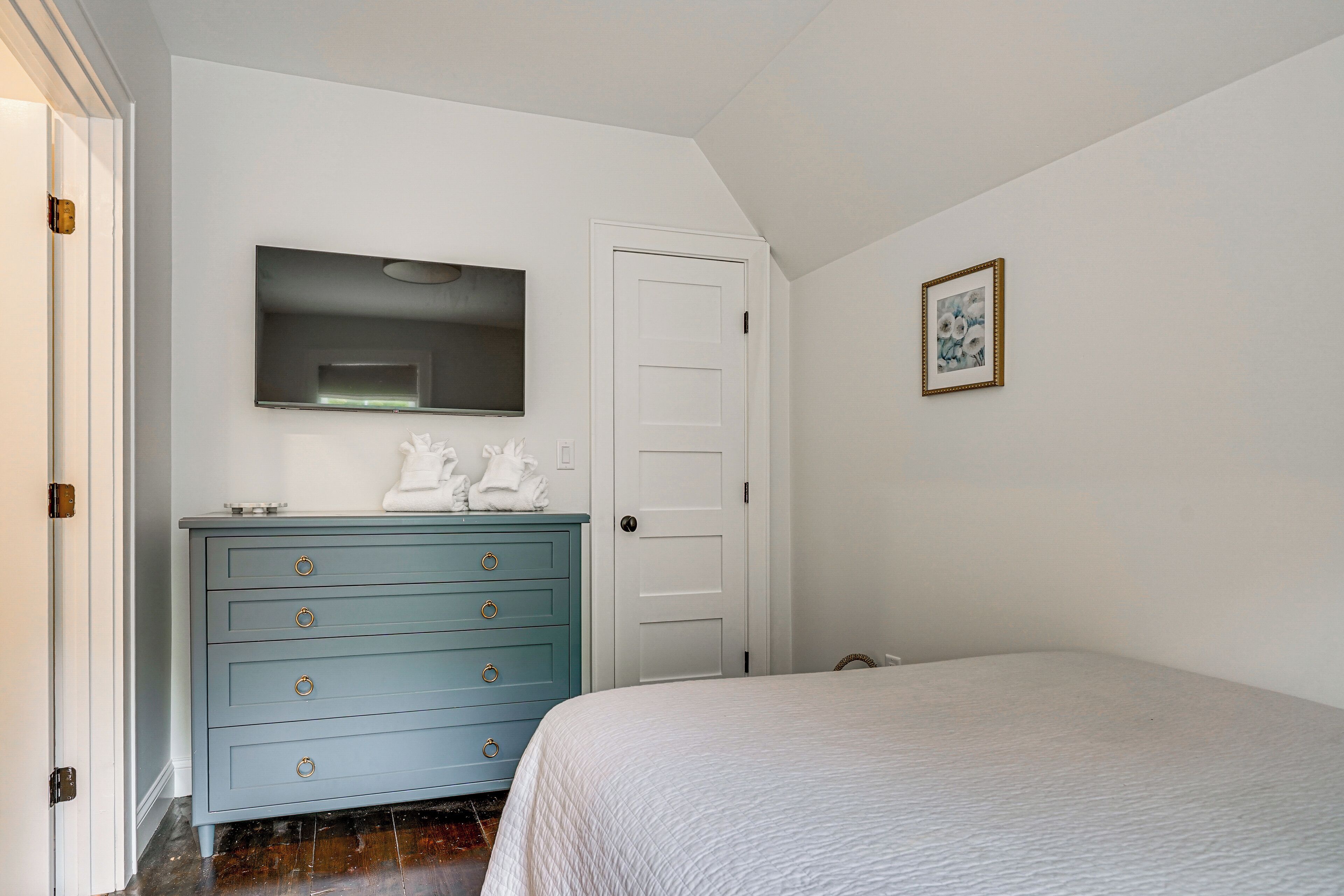A bedroom with a bed, a dresser with drawers, a door, and a framed picture on the wall.