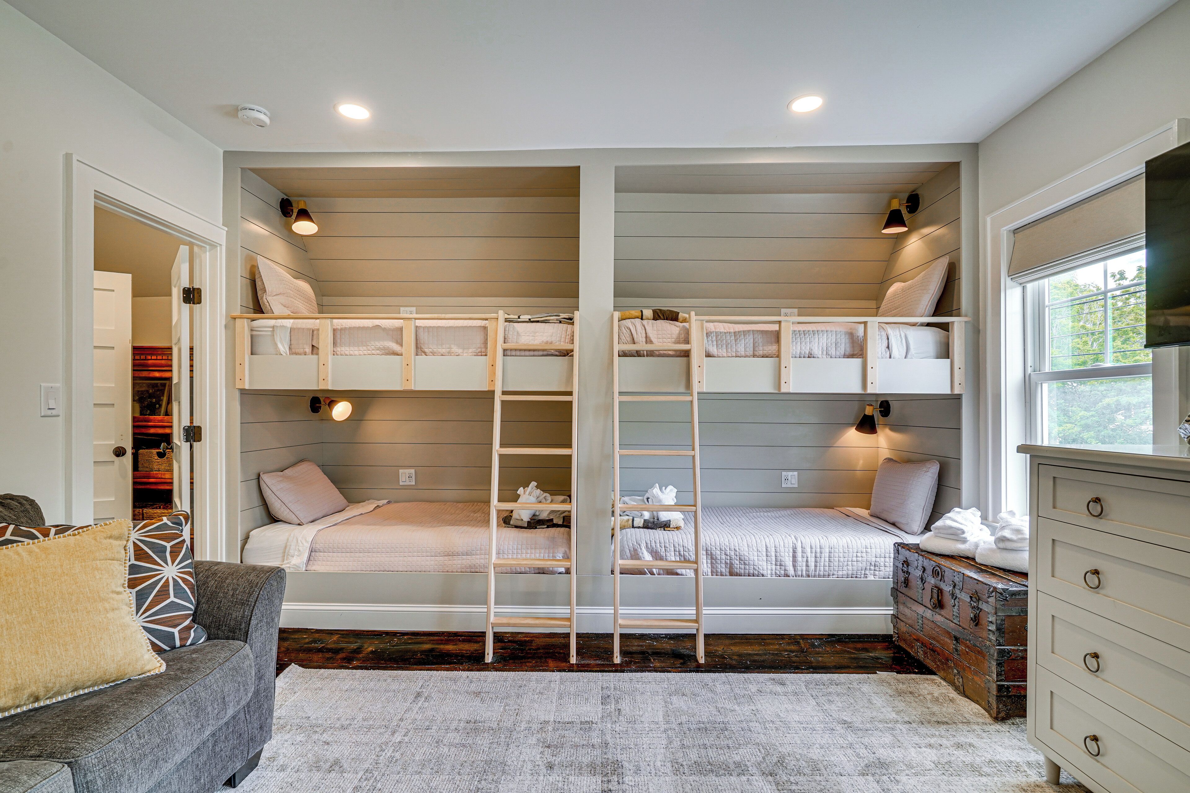 A room with bunk beds, a ladder, a dresser, and a window.