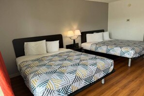 A hotel room with two beds, each with a patterned bedspread, a nightstand with a lamp, and a wooden floor.