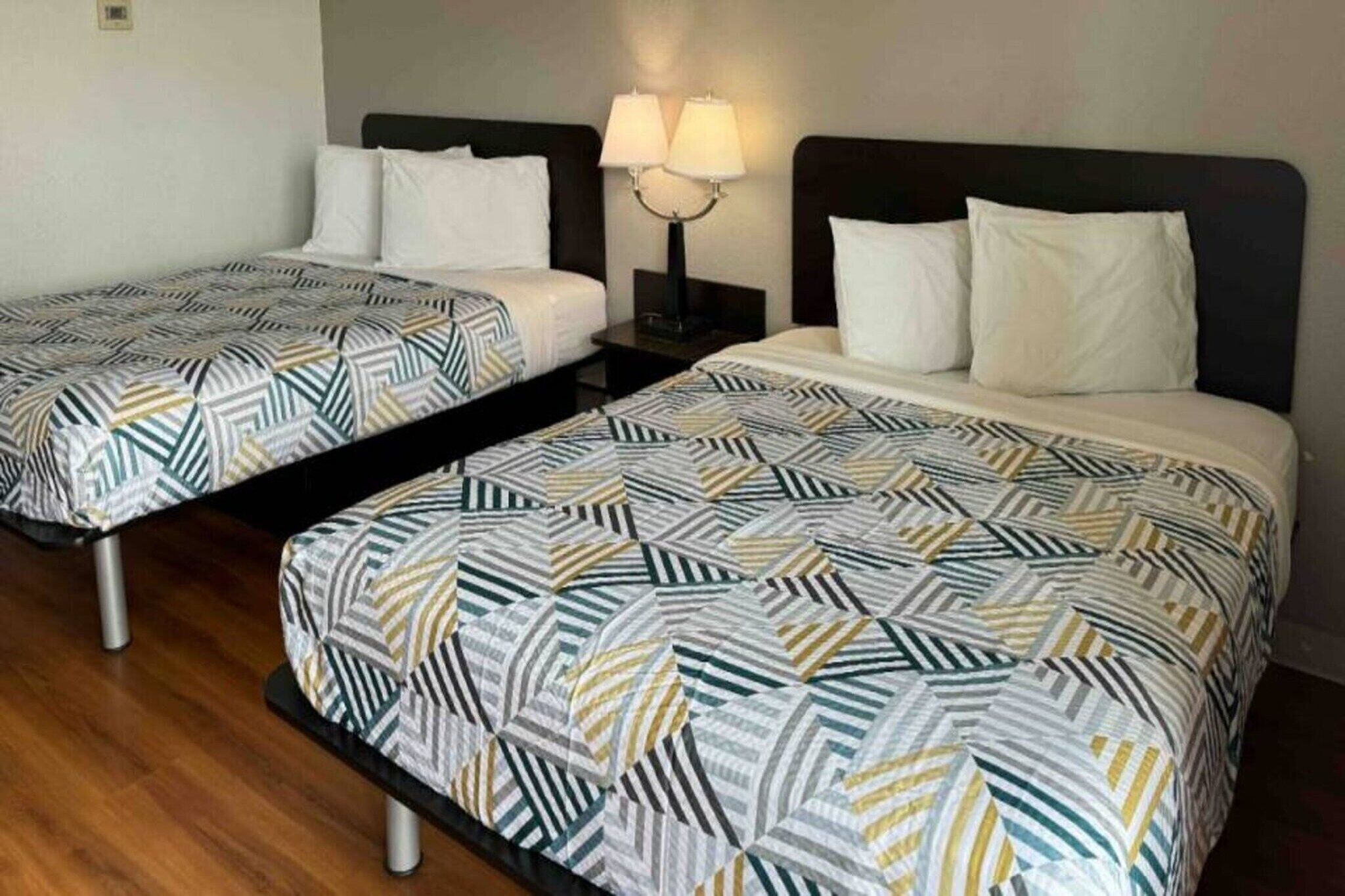 Zwei Doppelbetten mit gemusterten Bettbezügen, ein Nachttisch mit Lampe und ein Holzboden.