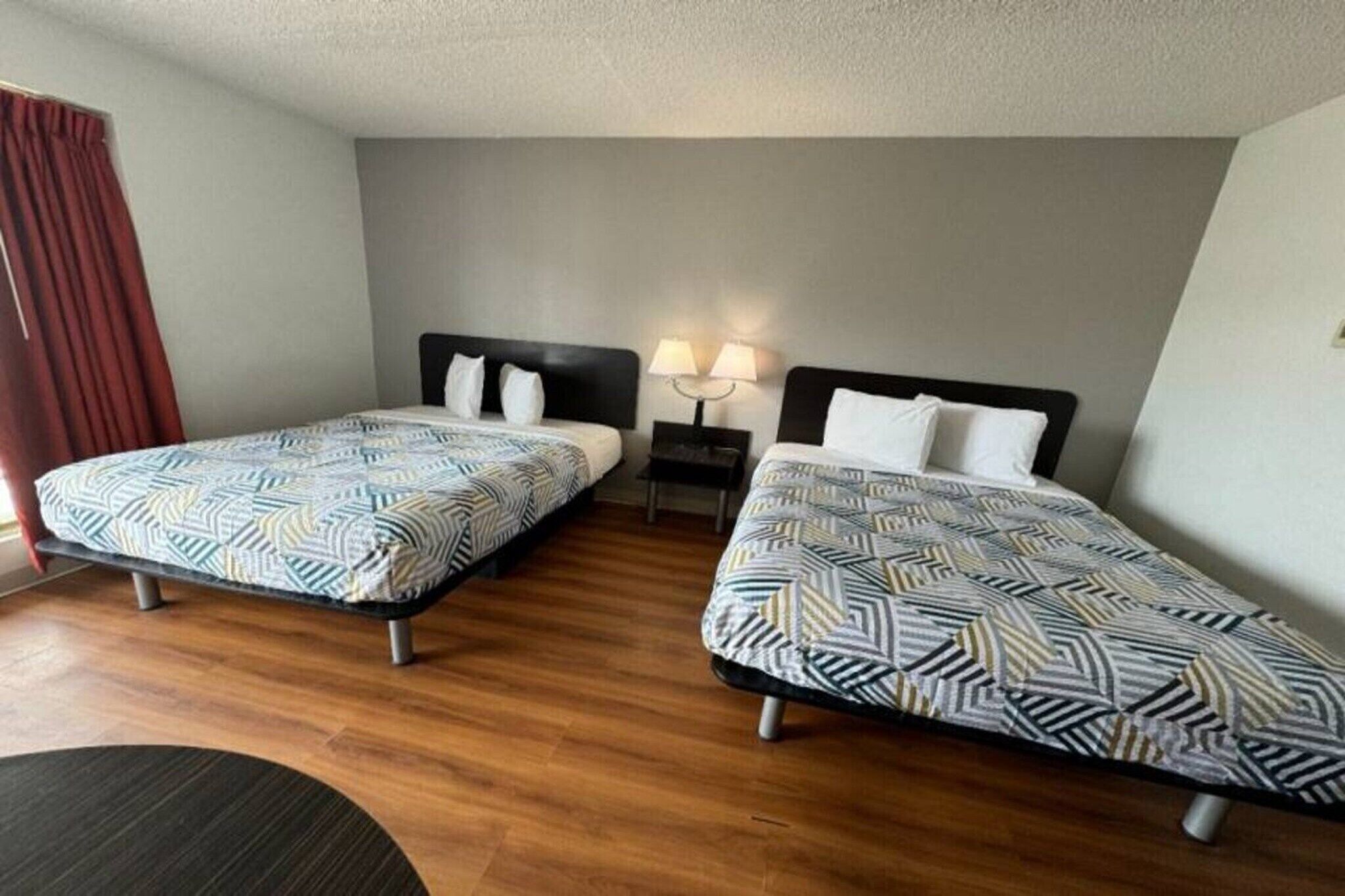 Una habitación de hotel con dos camas individuales, una mesita de noche con lámpara y suelo de madera.