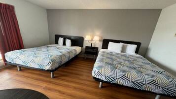 Una habitación de hotel con dos camas individuales, una mesita de noche con lámpara y suelo de madera.