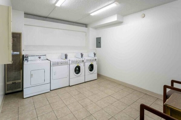 A laundry room with four washing machines and dryers, a ventilation system, and a tiled floor.