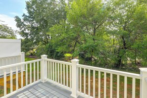 Une terrasse en bois avec des rampes blanches donnant sur une zone herbeuse bordée d’arbres.