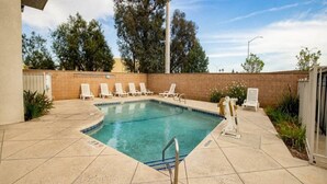 A rectangular swimming pool with a tiled deck, surrounded by white lounge chairs, a metal ladder, and a brick wall. - 1 QUEEN BED | NON-SMOKING, MINI FRIDGE (ONTARIO)
