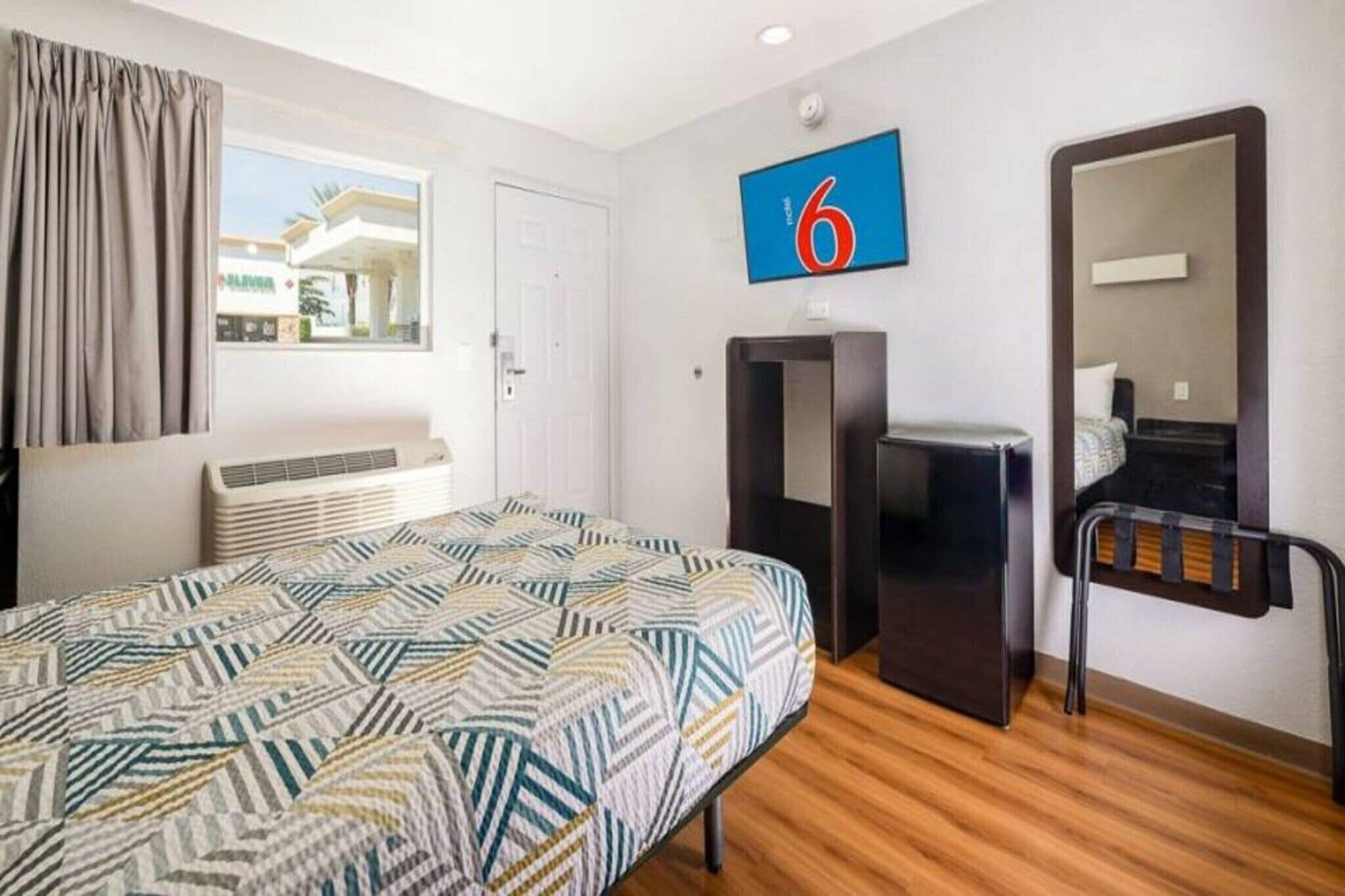A hotel room with a bed, a desk, a chair, a mirror, and a window with curtains.