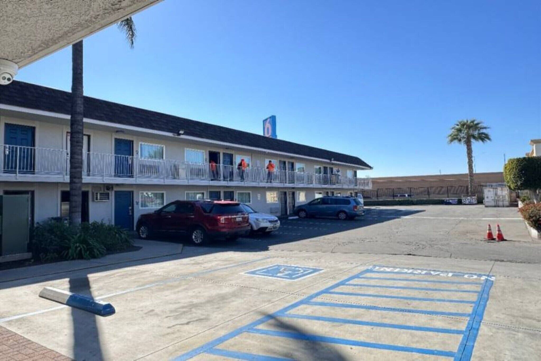 A motel with a parking lot, a building with a balcony, and a palm tree.