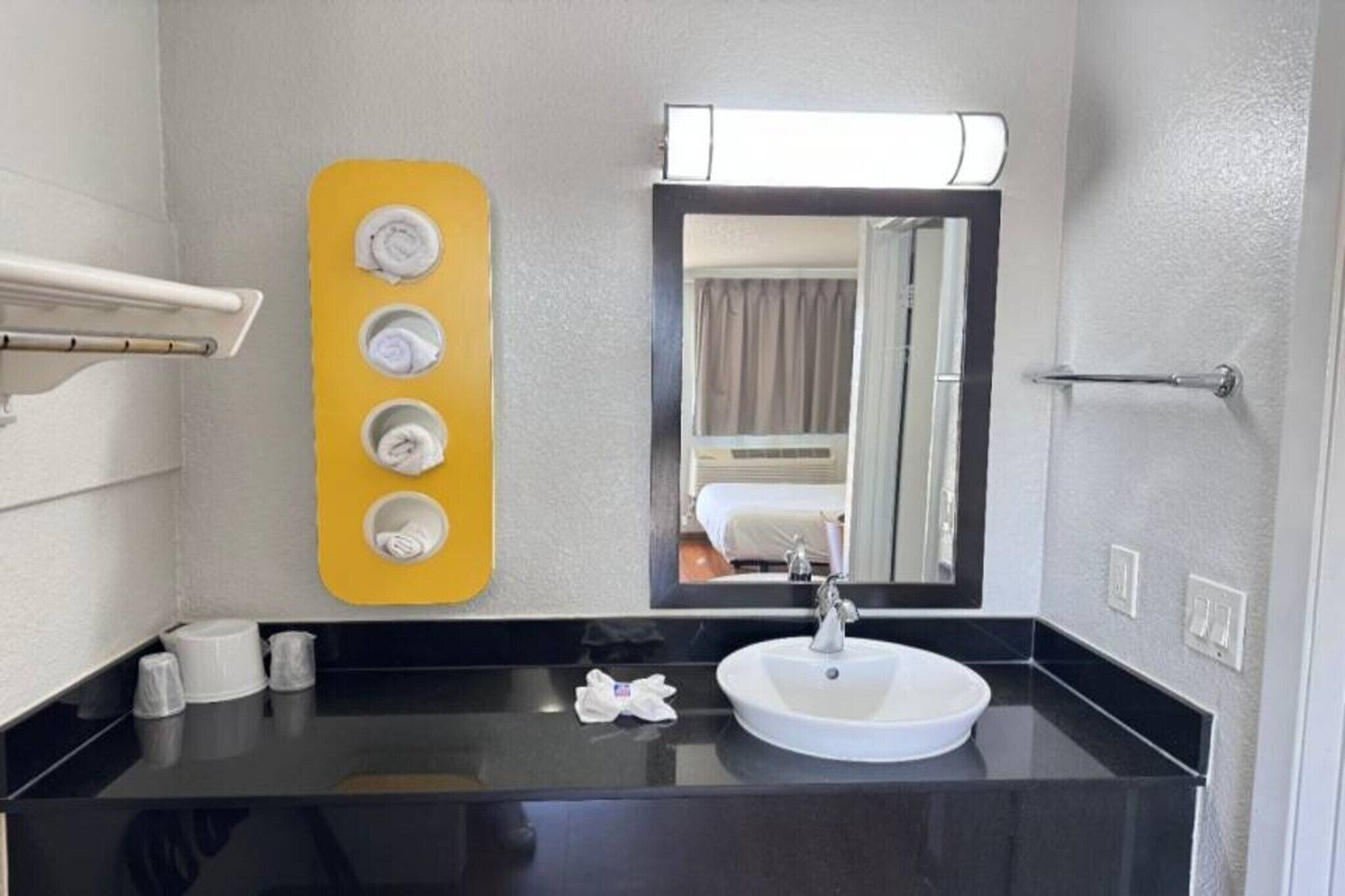 A bathroom with a black countertop, a white sink, a mirror, and a yellow towel rack with four towels.