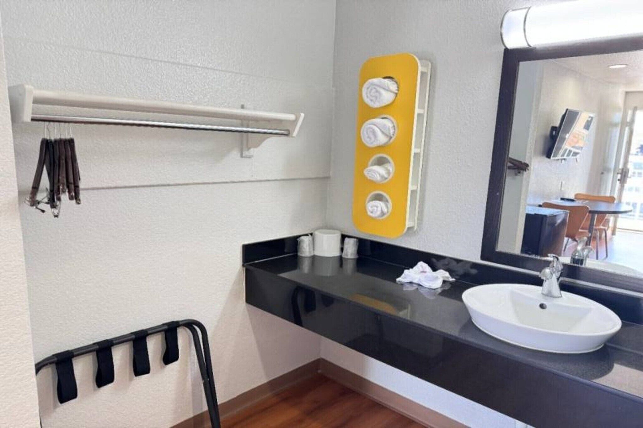 A bathroom with a black countertop, a white sink, a mirror, and a towel rack.
