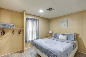 A bedroom with a bed, a nightstand, a lamp, a window with curtains, and a wall-mounted shelf with folded towels. - 5-Unit Retreat Near World Equestrian Center & HITS (Morriston)
