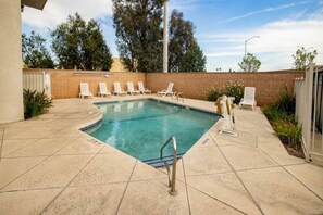 A rectangular swimming pool with a tiled deck, surrounded by white lounge chairs, a metal ladder, and a brick wall. - 2 FULL BEDS | NON-SMOKING, MINI FRIDGE (ONTARIO)