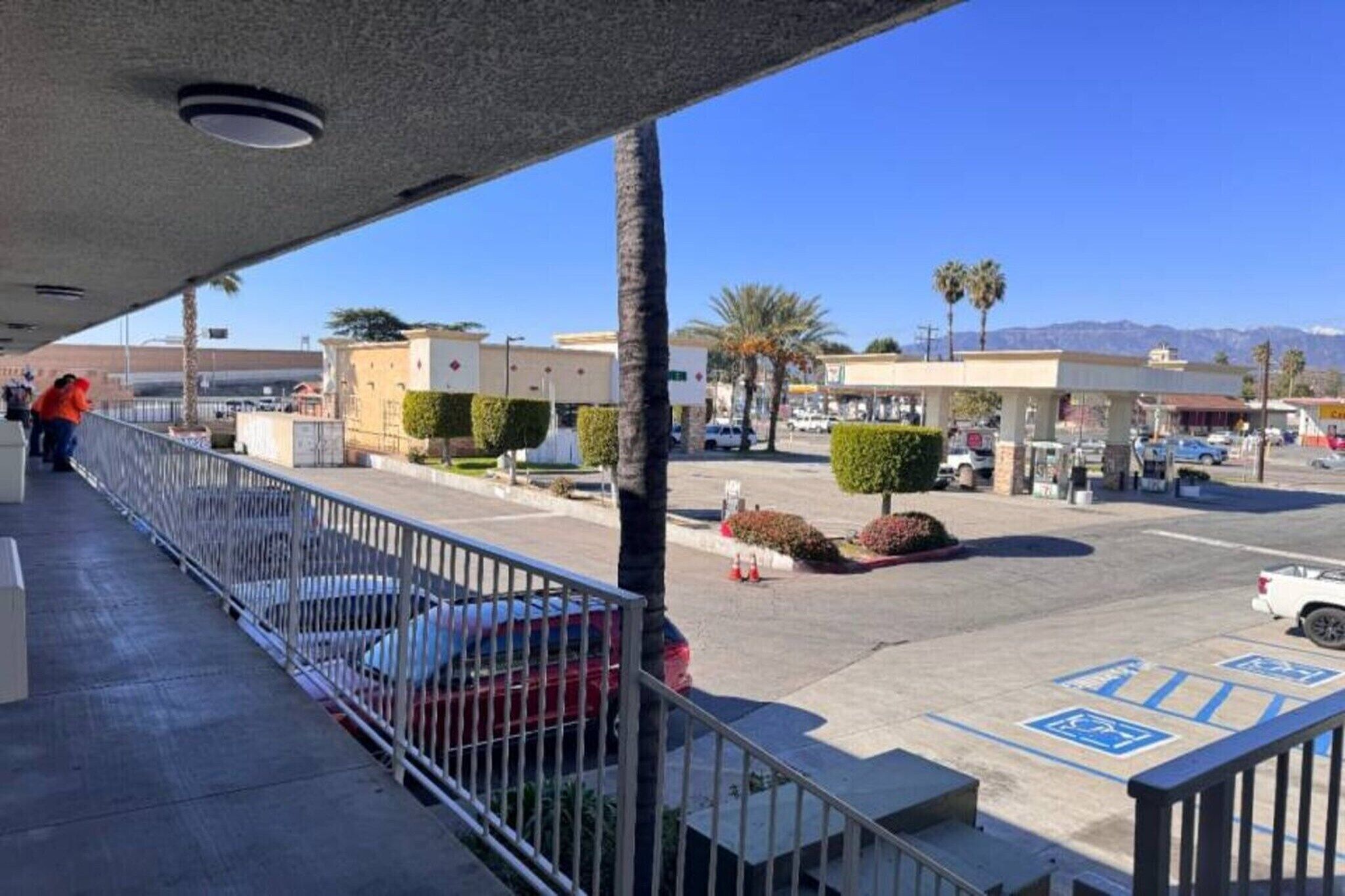 An outdoor area with a covered walkway, a parking lot, and a gas station in the background.