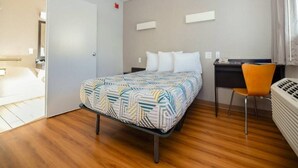 A hotel room with a bed, a desk, a chair, and a radiator.