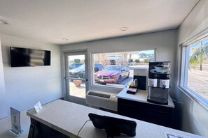 A room with a desk, a coffee machine, a TV mounted on the wall, and a window with a view of parked cars and a building outside. - 2 FULL BEDS | NON-SMOKING, MINI FRIDGE (ONTARIO)