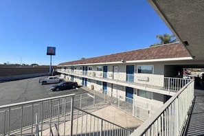 A motel with a parking lot, a sign indicating the number 6, and a building with a flat roof. - 2 FULL BEDS | NON-SMOKING, MINI FRIDGE (ONTARIO)