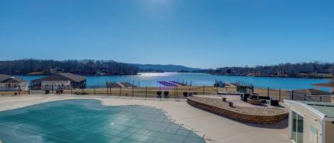 A swimming pool with a glass enclosure, a waterfront view, and a small building with a sign.