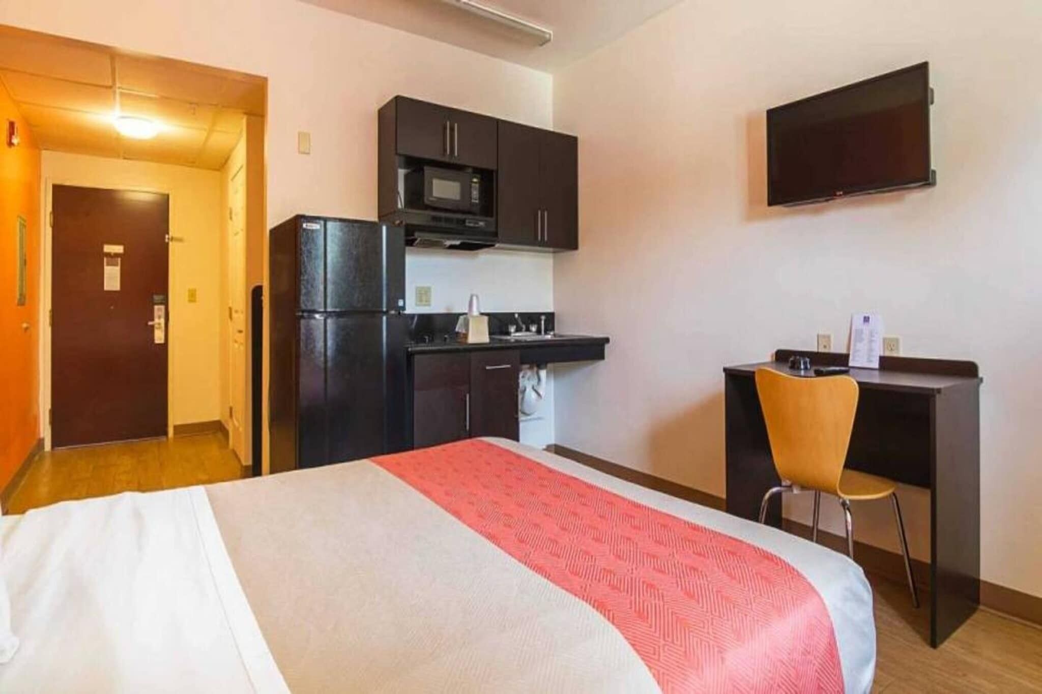 A hotel room with a bed, a desk, a chair, a microwave, and a television.