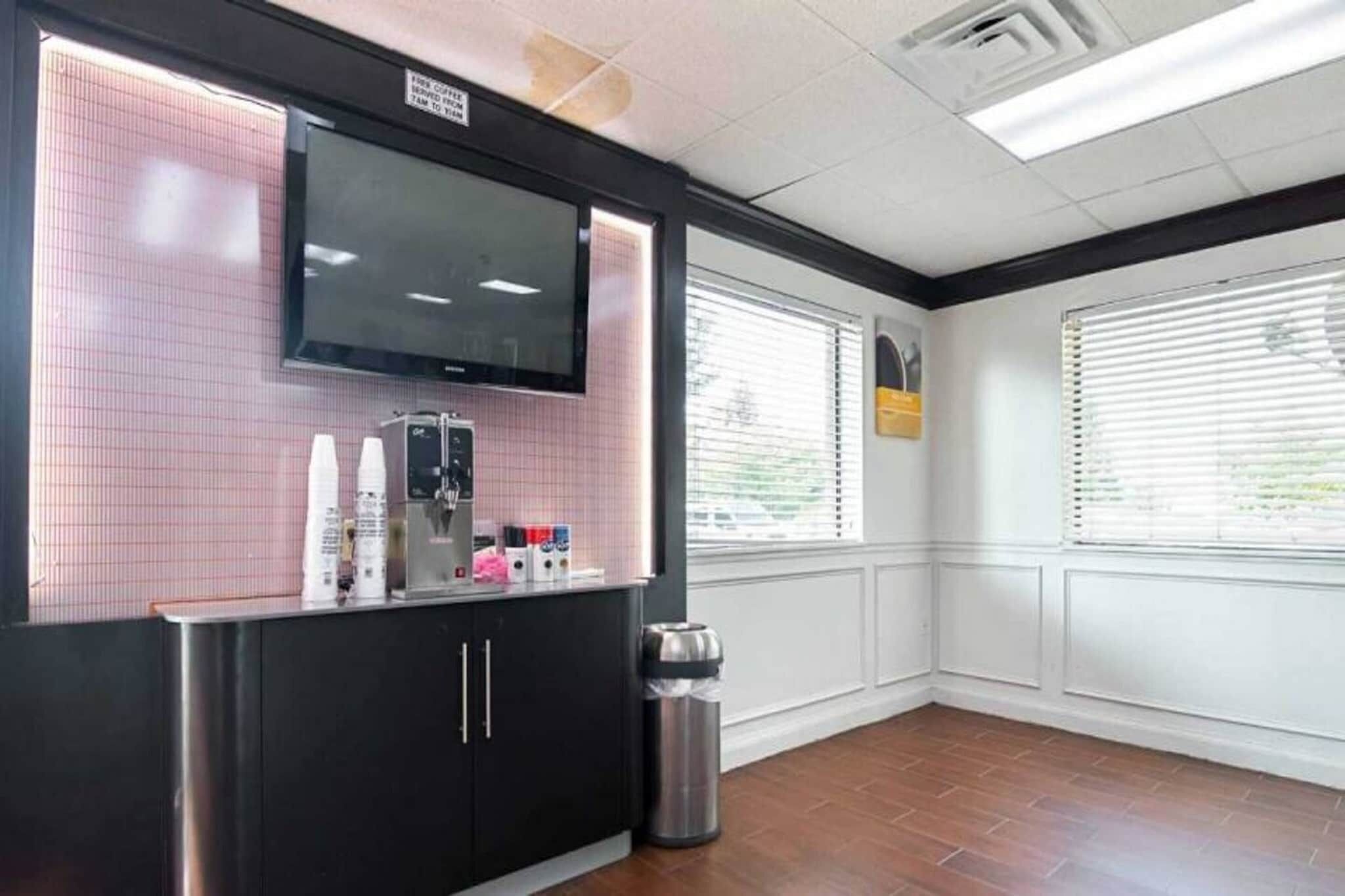 Un espace café propre et moderne, équipé d’un téléviseur à écran plat, d’une poubelle et d’une fenêtre avec des stores.