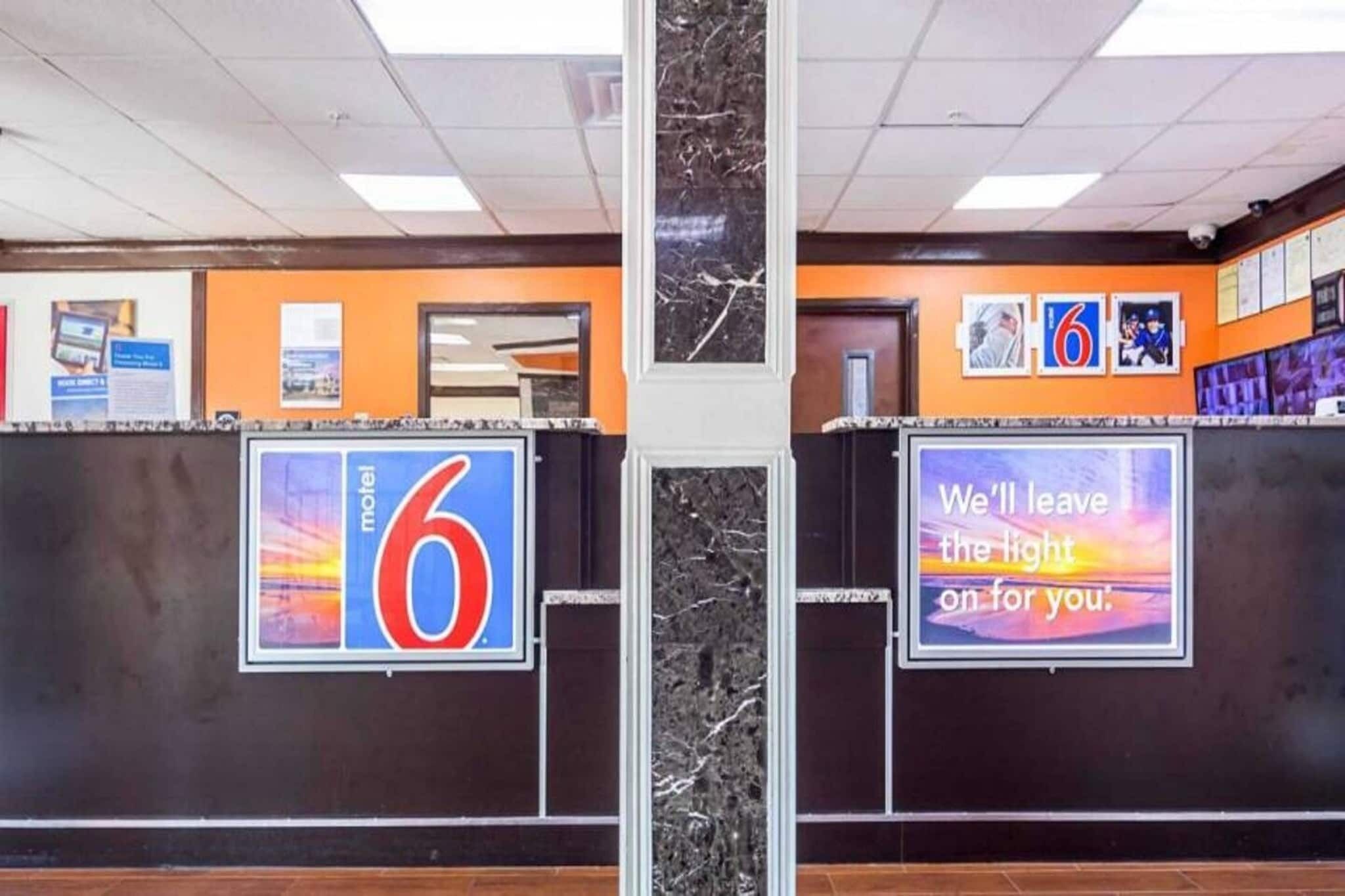 Un comptoir d’accueil avec une enseigne indiquant « Motel 6 » et une autre qui dit : « Nous laisserons la lumière allumée pour vous. »