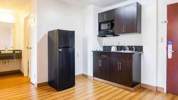 Uma cozinha compacta com geladeira, micro-ondas e armários escuros.