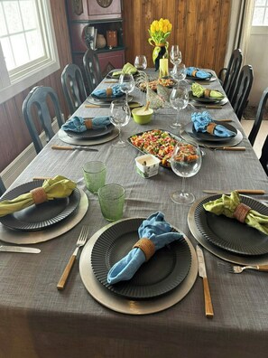 Ein Esstisch gedeckt mit Tellern, Gläsern und Besteck, mit einer Blumenvase und einer Salatschüssel.
