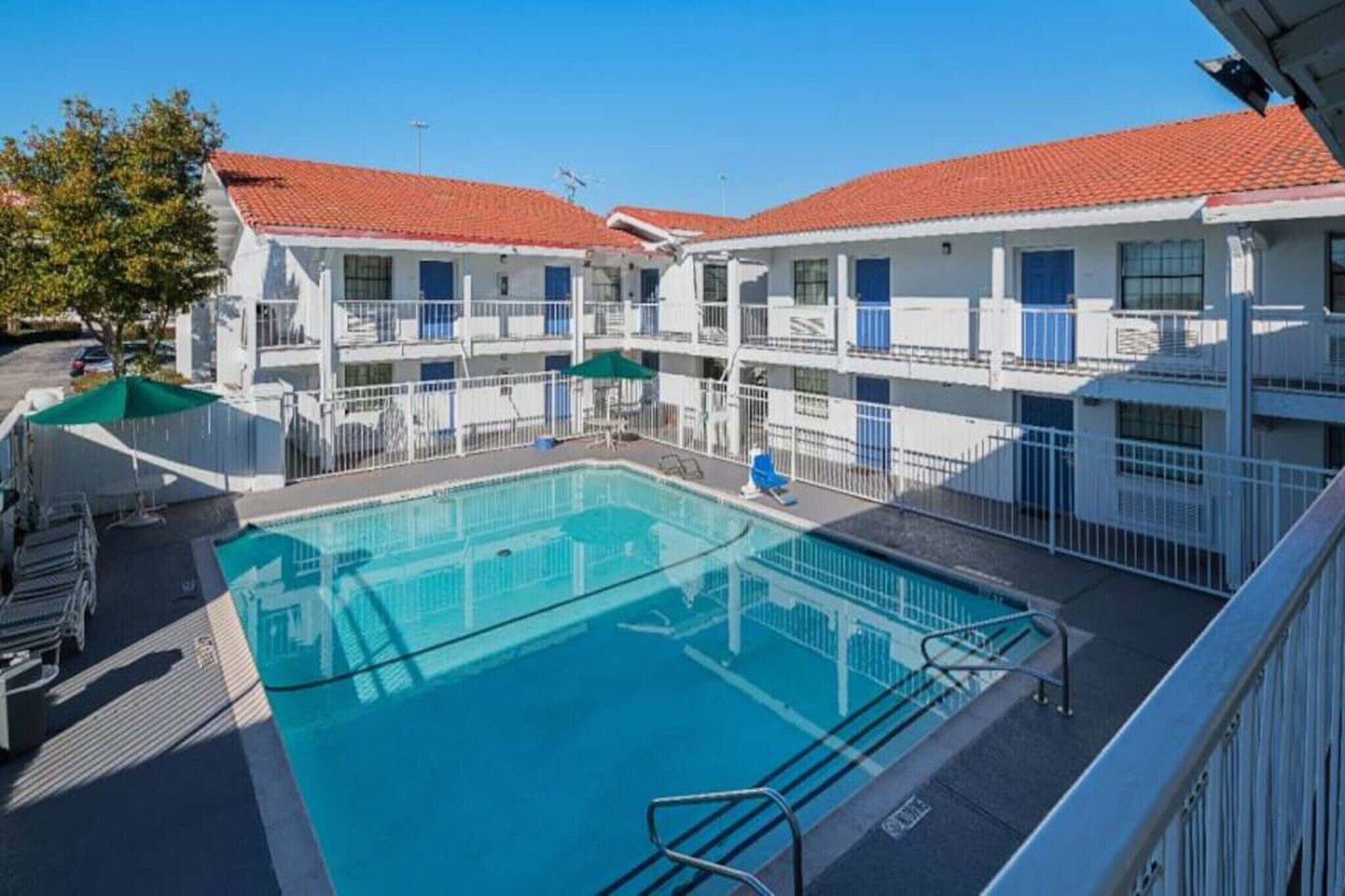 A hotel with a central swimming pool, multiple balconies, and a red-tiled roof.