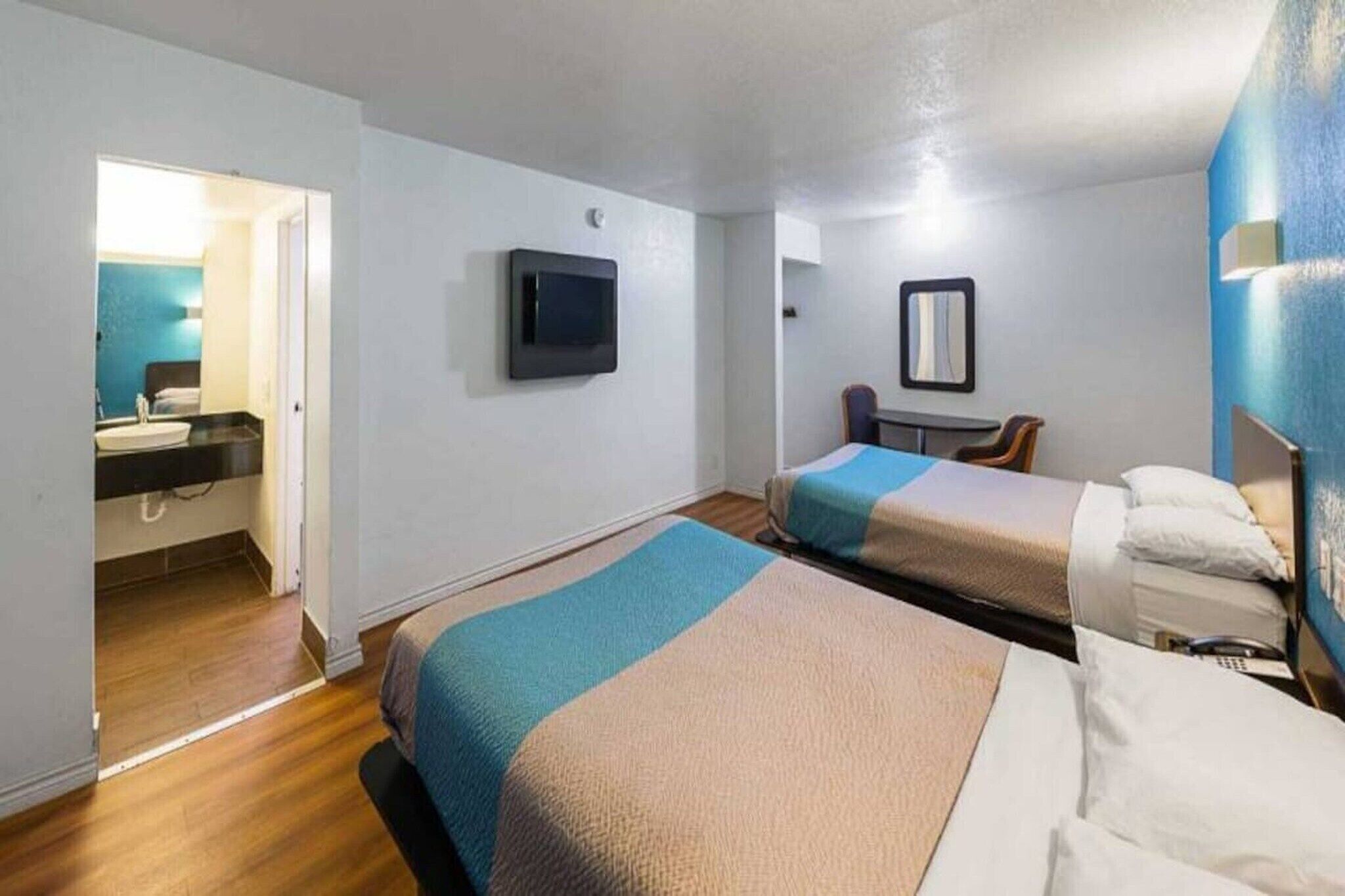 A hotel room with two beds, a TV, a small table, and a mirror.