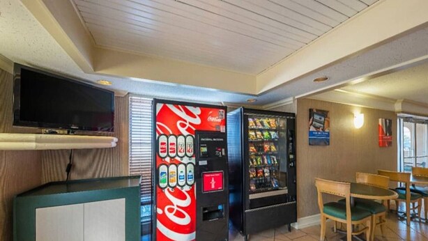 A room with a television, a Coca-Cola vending machine, a snack vending machine, and a wooden table with chairs. - 2 FULL BEDS | NON-SMOKING (Grand Prairie)