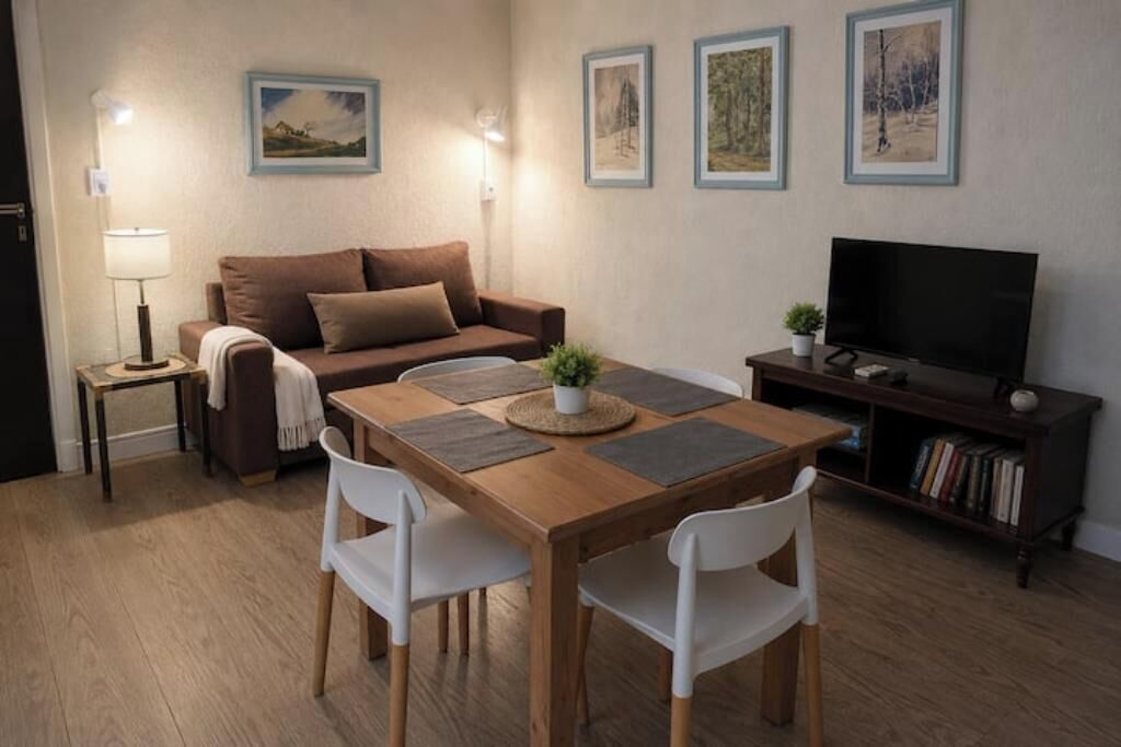 Una sala de estar amoblada con sofá, televisor, mesa de comedor con sillas y cuadros en la pared.