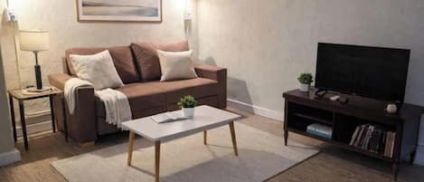 A living room with a sofa, a coffee table, a TV stand with a flat-screen TV, a lamp, and a framed picture on the wall.