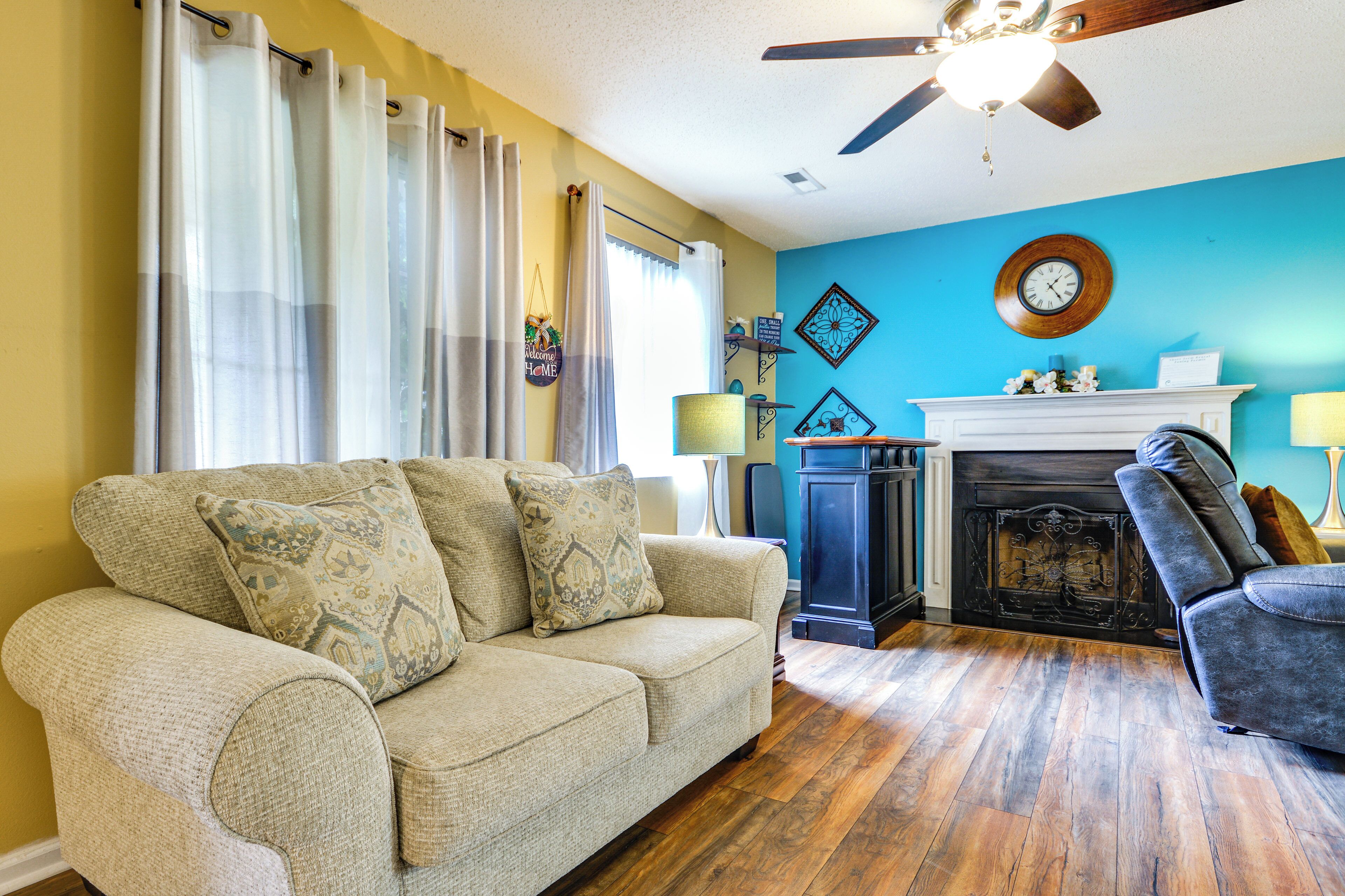 A living room with a sofa, a chair, a fireplace, and a ceiling fan.