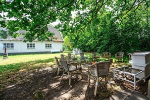 A backyard with outdoor furniture, a barbecue grill, and a house in the background.