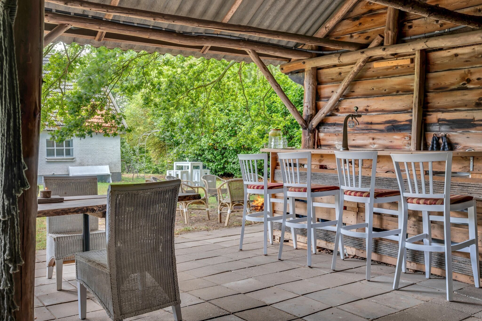 An outdoor patio with wooden tables and chairs, a fire pit, and a view of a green landscape.
