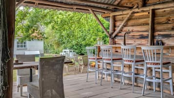 An outdoor patio with wooden tables and chairs, a fire pit, and a view of a green landscape.
